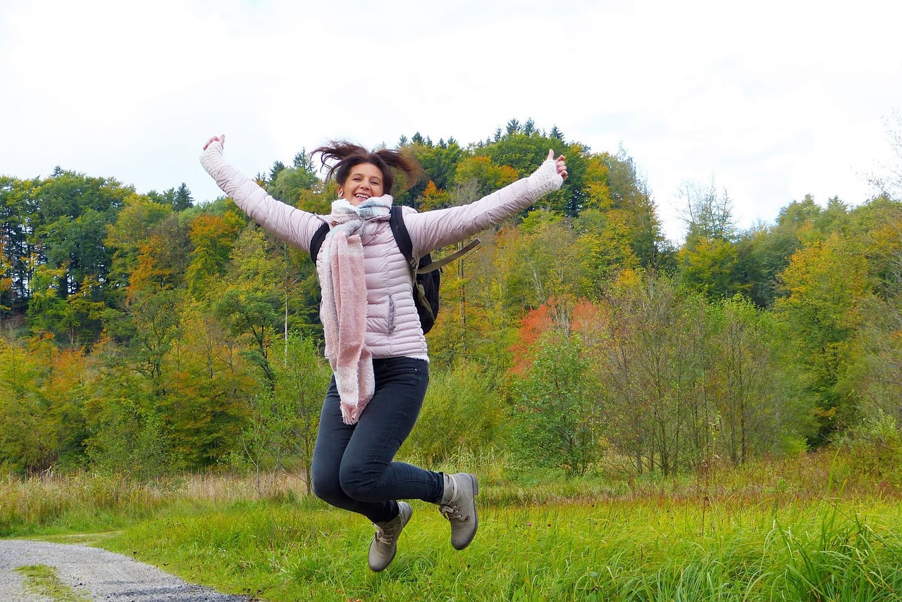 A woman jumping for joy outside wearing a scarf, jeans and boots