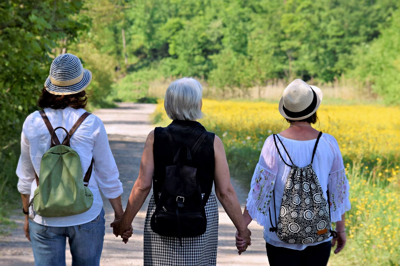 Three older women walking together hand in hand on a sunny day